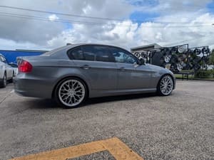  Grey BMW 3 Series sedan fitted with silver multi-spoke alloy wheels outside a wheel shop.