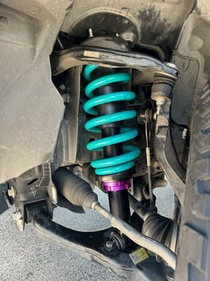  Close-up of upgraded front suspension coilover with bright blue spring and adjustable shock.
