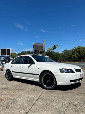  White Ford Falcon sedan lowered on glossy black aftermarket alloy wheels.