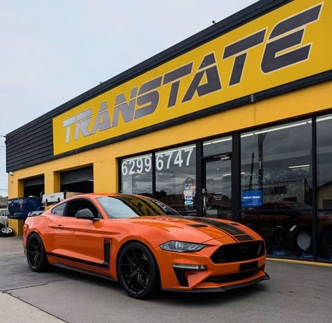 Orange Ford Mustang with black racing stripes outside the Transtate workshop 